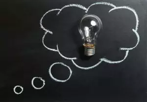 Light bulb laying on chalkboard with drawn thought bubble, symbolizing creative ideas.